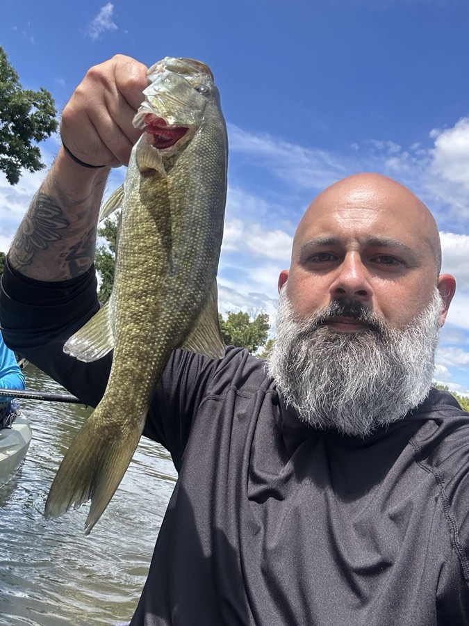 A bearded man holding up a smallmouth bass from the boat